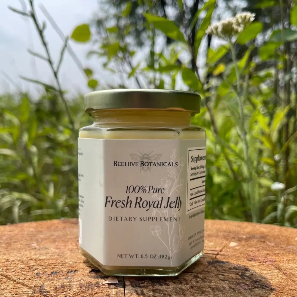 Jar of fresh royal jelly on wooden surface outdoors with natural greenery background