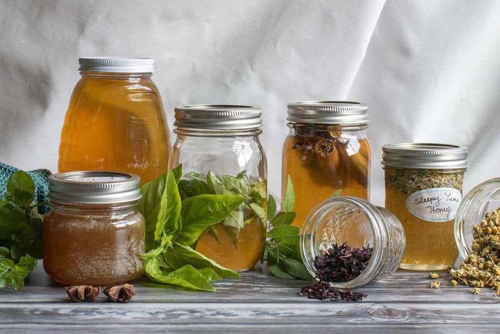 Homemade fermented honey with fresh herbs and dried flowers in glass jars